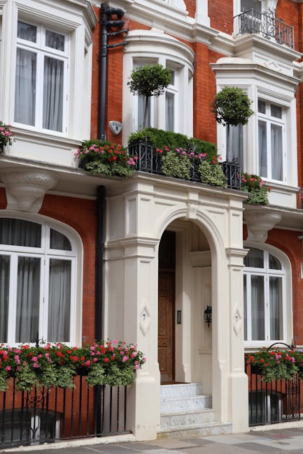 The image showcases the exterior of a classic Victorian-style townhouse with red brick walls and white decorative trim. The entrance features a wooden door beneath an elegant archway, flanked by white